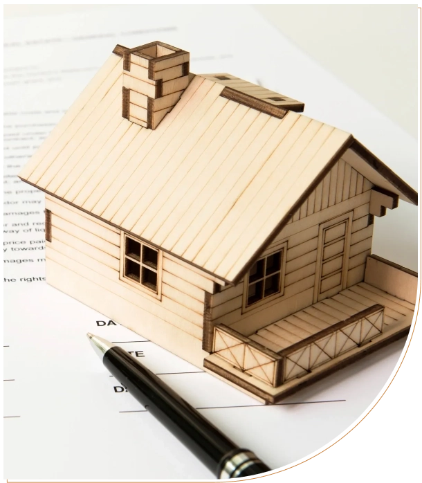 Wooden model of a house on architectural plans with a pen.