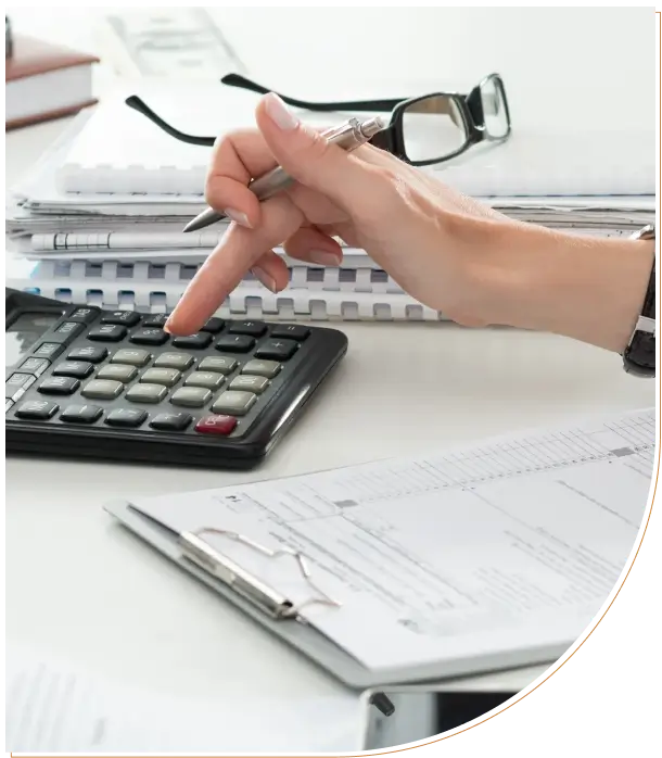 Person using calculator with paperwork and glasses nearby.